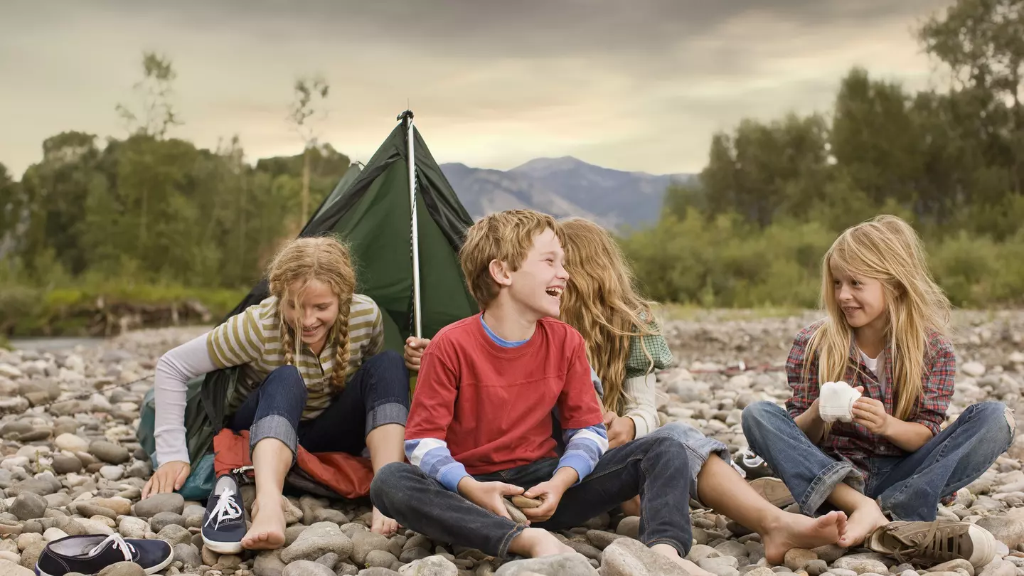 Brother and sisters playing in small tent on a rocky creek bank