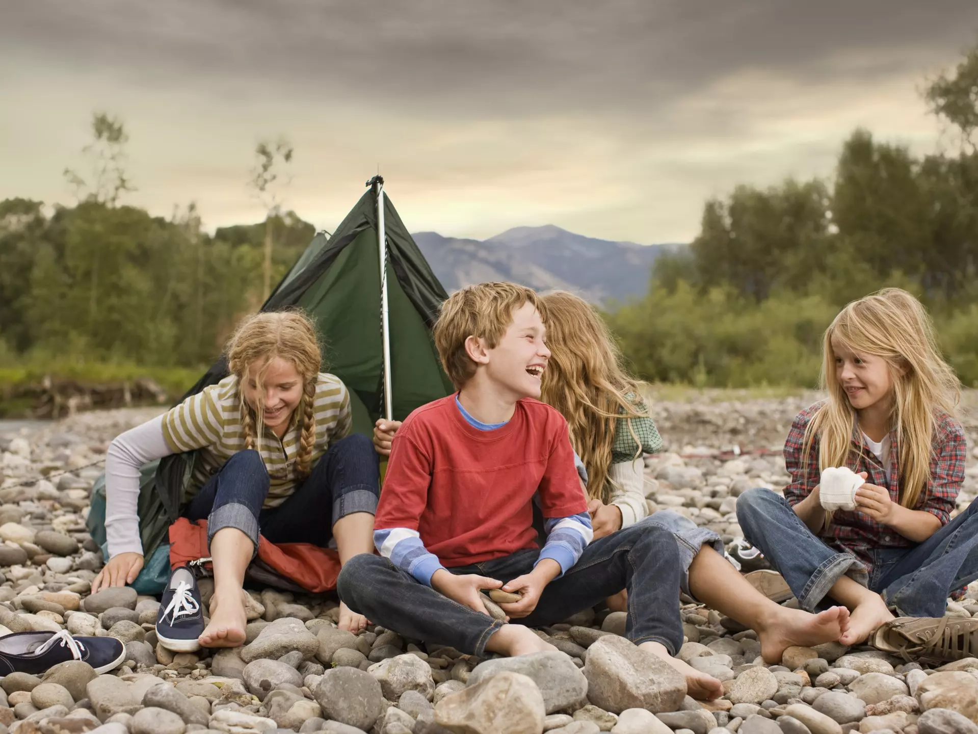 Brother and sisters playing in small tent on a rocky creek bank