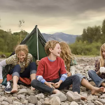 Brother and sisters playing in small tent on a rocky creek bank