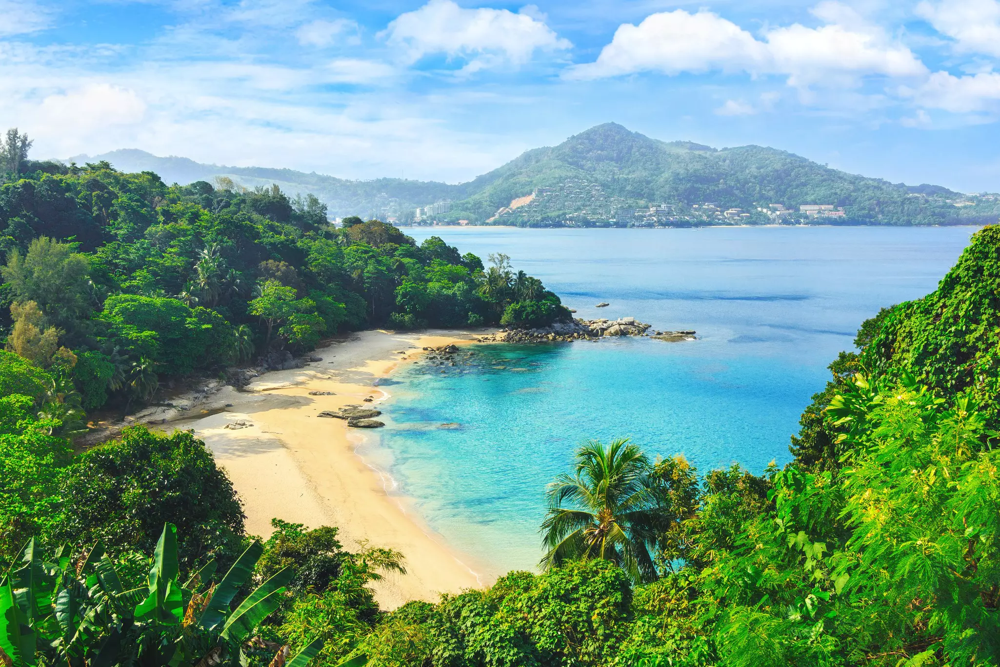 An empty beach with golden sand and a turquoise cove seen through the jungle.