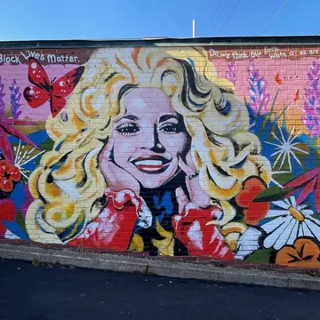 Large mural of country legend Dolly Parton surrounded by pink and purple flowers