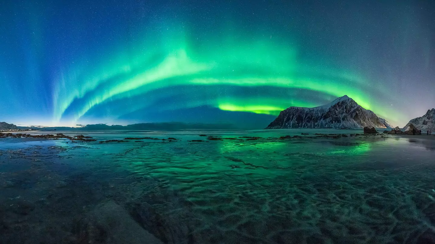 The green lights of the Aurora Borealis light up the night sky above Skagsanden Beach, Norway.