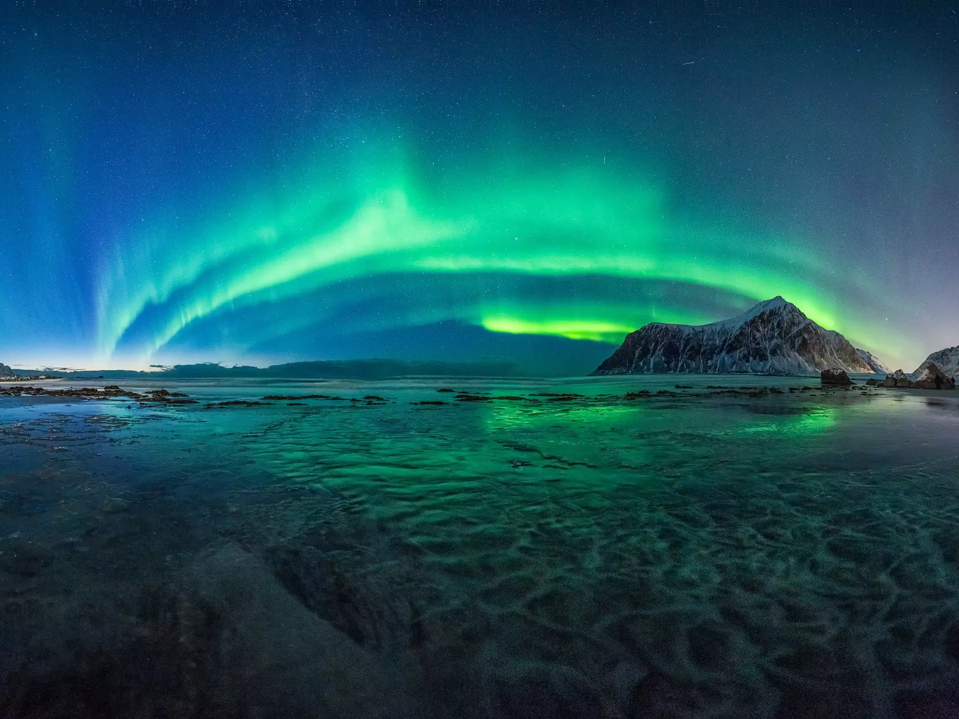 The green lights of the Aurora Borealis light up the night sky above Skagsanden Beach, Norway.