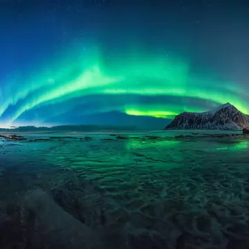The green lights of the Aurora Borealis light up the night sky above Skagsanden Beach, Norway.