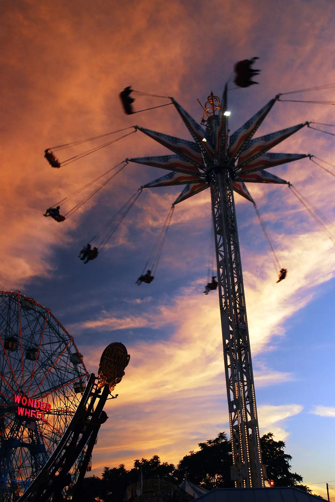 An elevated swing ride in motion and a ferris wheel at sunset in an amusement park