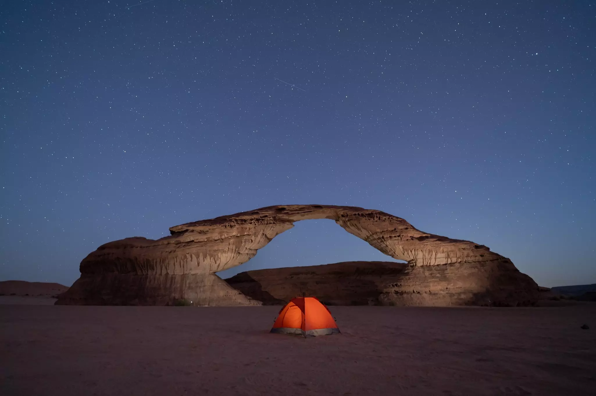 An orange tent by a rock formation at night under stars.
