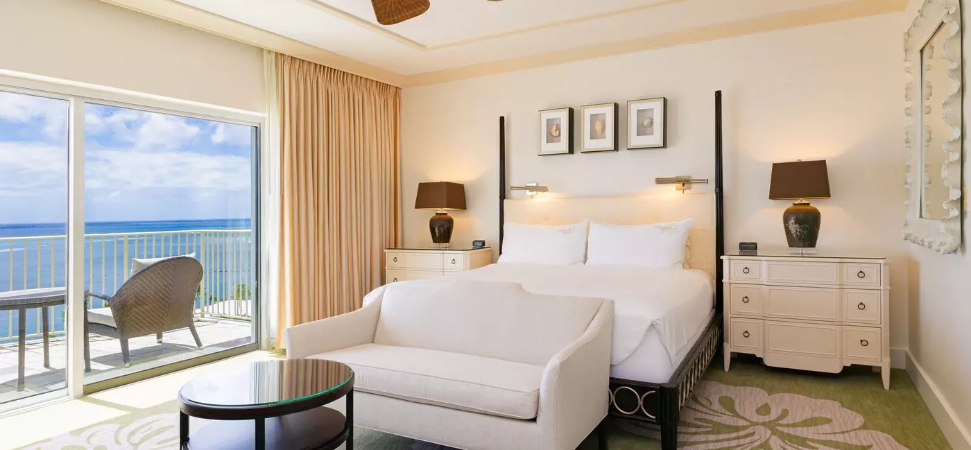 A large bed in a hotel suite with ocean views off the balcony
