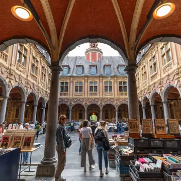 Shoppers and browsers wander around a secondhand book market within the covered arcade of a former stock exchange.