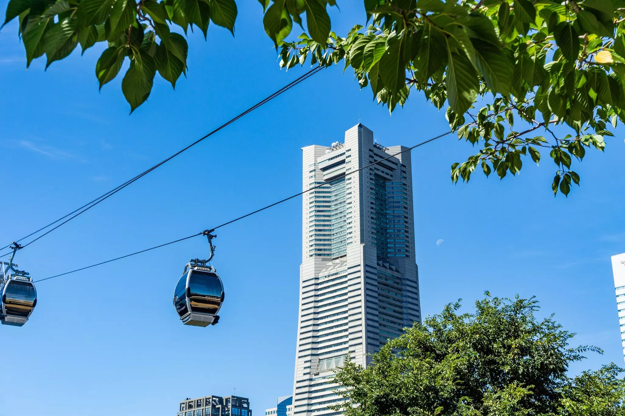 Wide shot of tall city skyscraper with aerial trams in foreground on a sunny day.