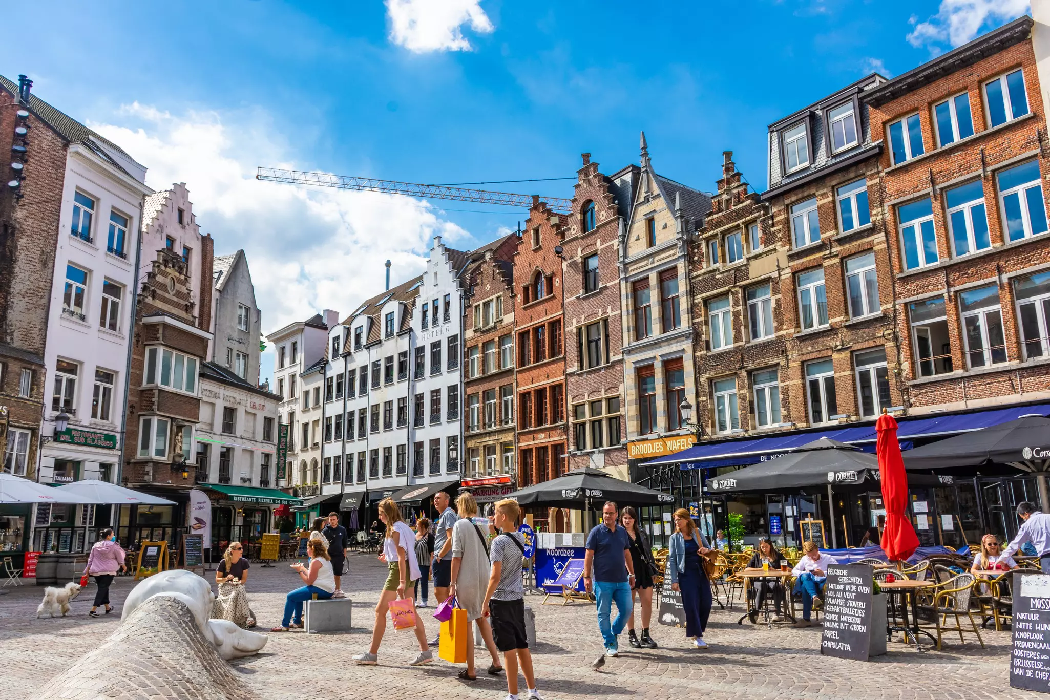 People wander through a city square lined with tall townhouses