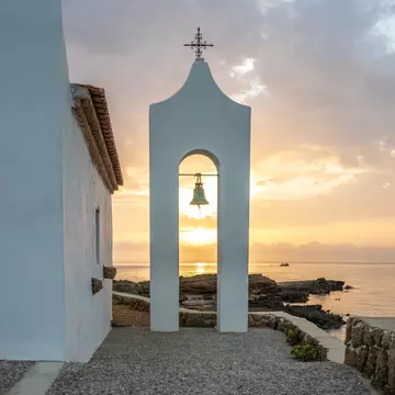 Small white church in the typical architectural style of Greece. She stands on a tree surrounded by the Mediterranean and in the sunrise.Chapel of Agios Nikolaos, Ionian Islands, Greece, License Type: media, Download Time: 2025-07-10T17:27:39.000Z, User: katelyn.perry_lonelyplanet, Editorial: false, purchase_order: 65050 - Digital Destinations and Articles, job: WIP, client: APP, other: Katelyn Perry