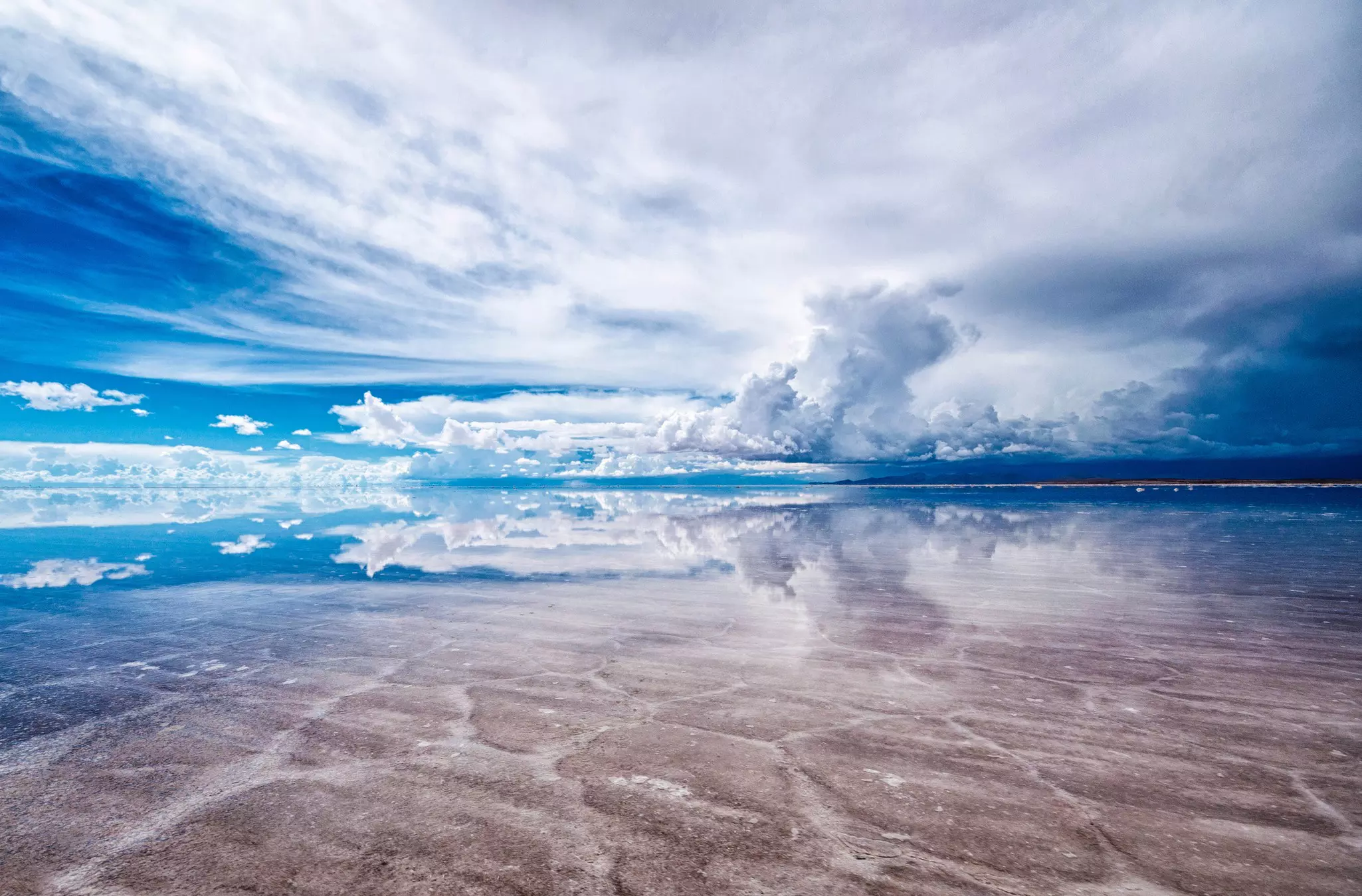 The blue sky and clouds reflected in the flat damp surface of vast salt flats.