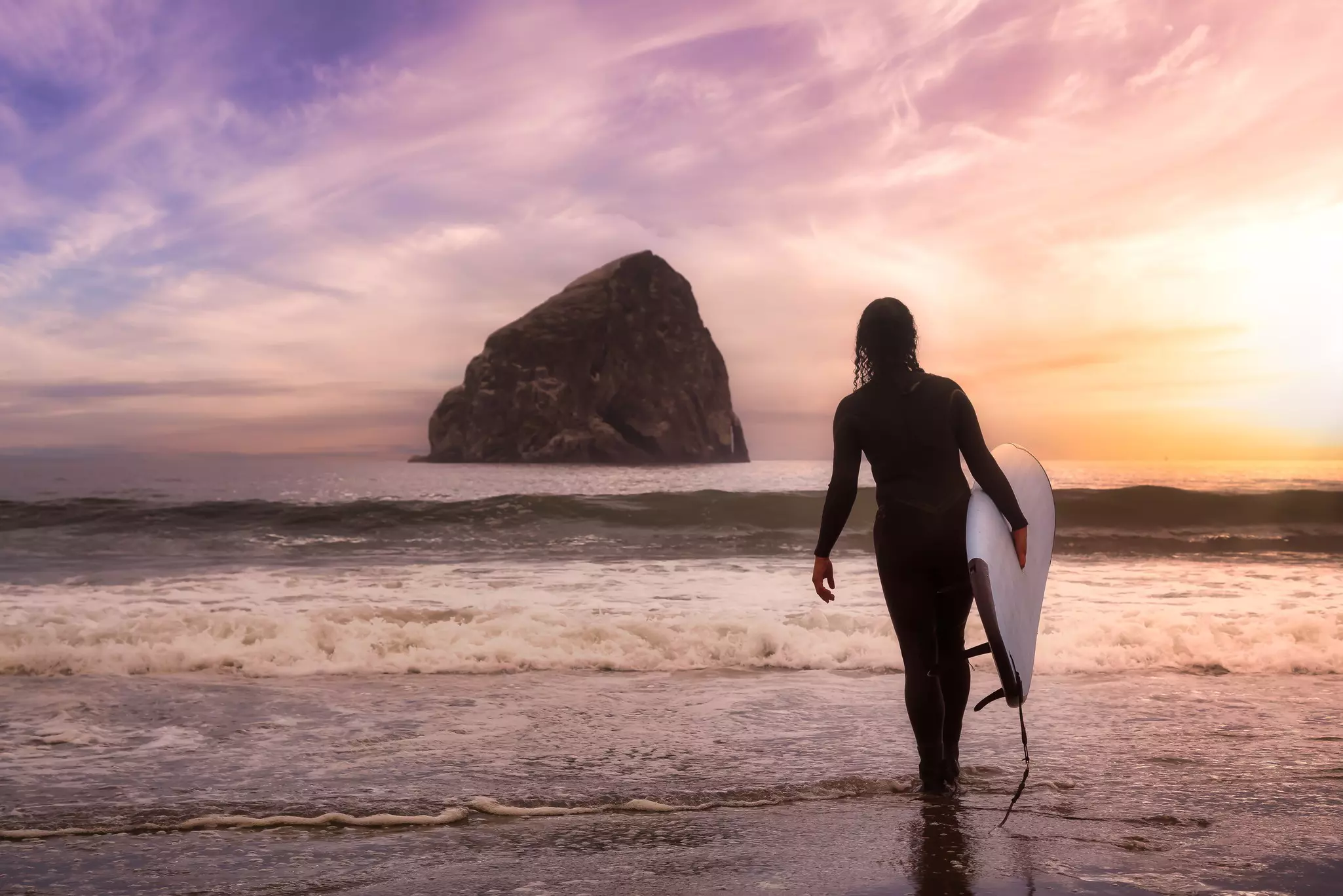 Girl with a Surf Board is going surfing in the Ocean. Colorful Sunset Sky. Taken in Pacific City, Oregon Coast, United States of America.