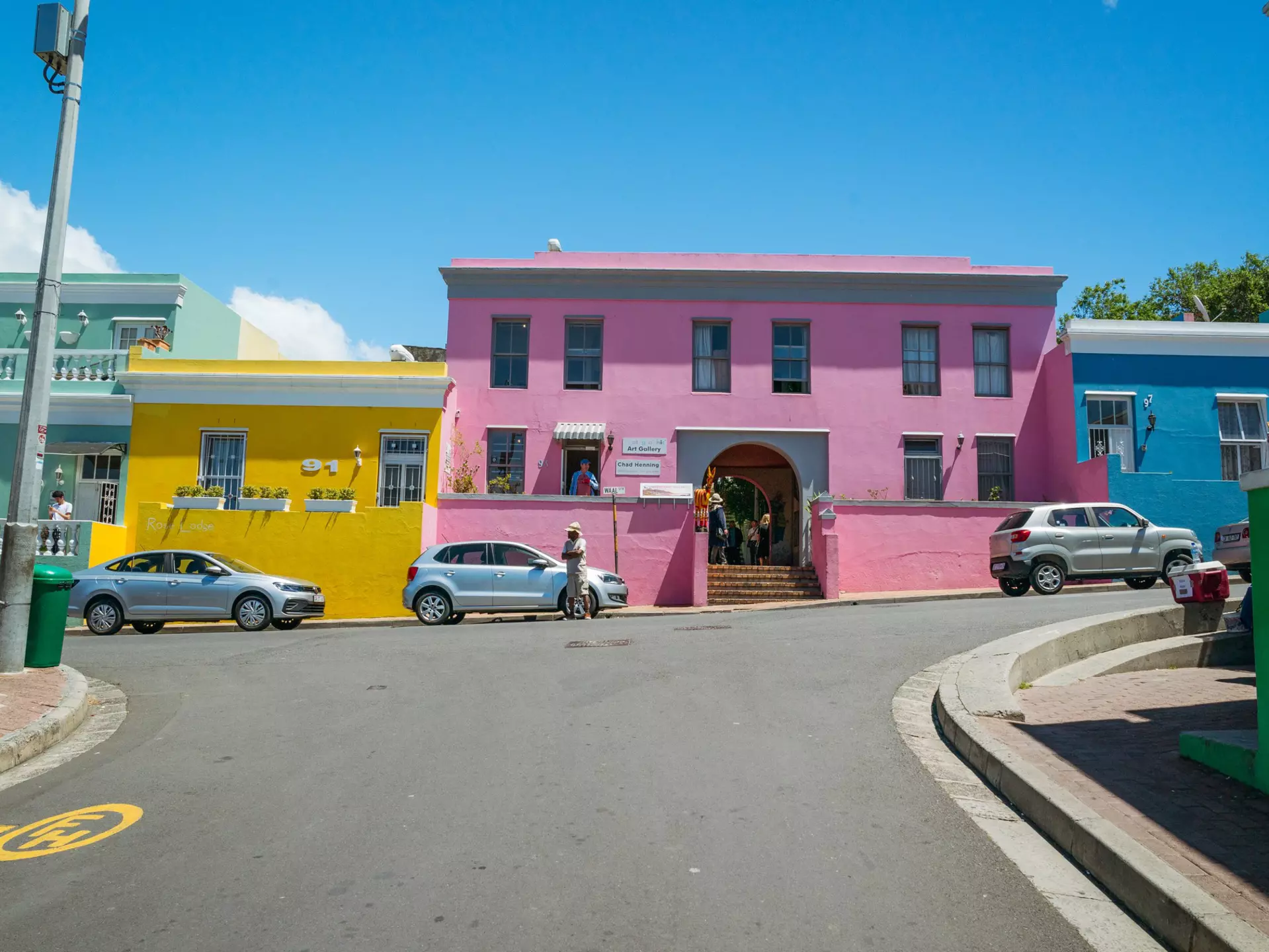Pink, yellow, green, and blue houses along a roadway on a sunny day.