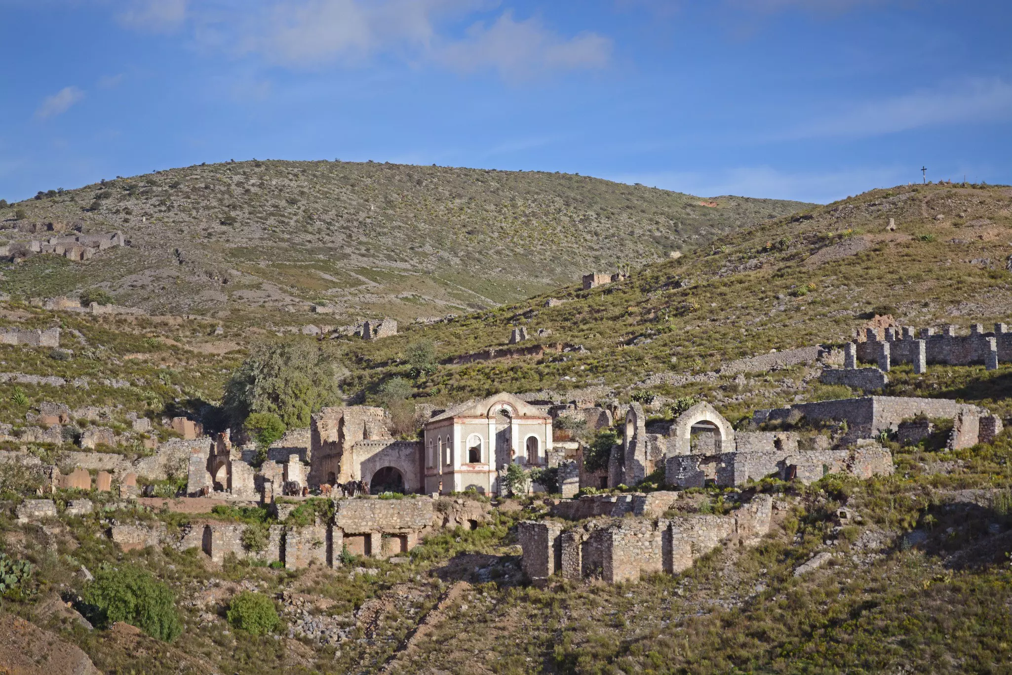 A cluster of buildings and old walls, some in ruins, on a hillside 