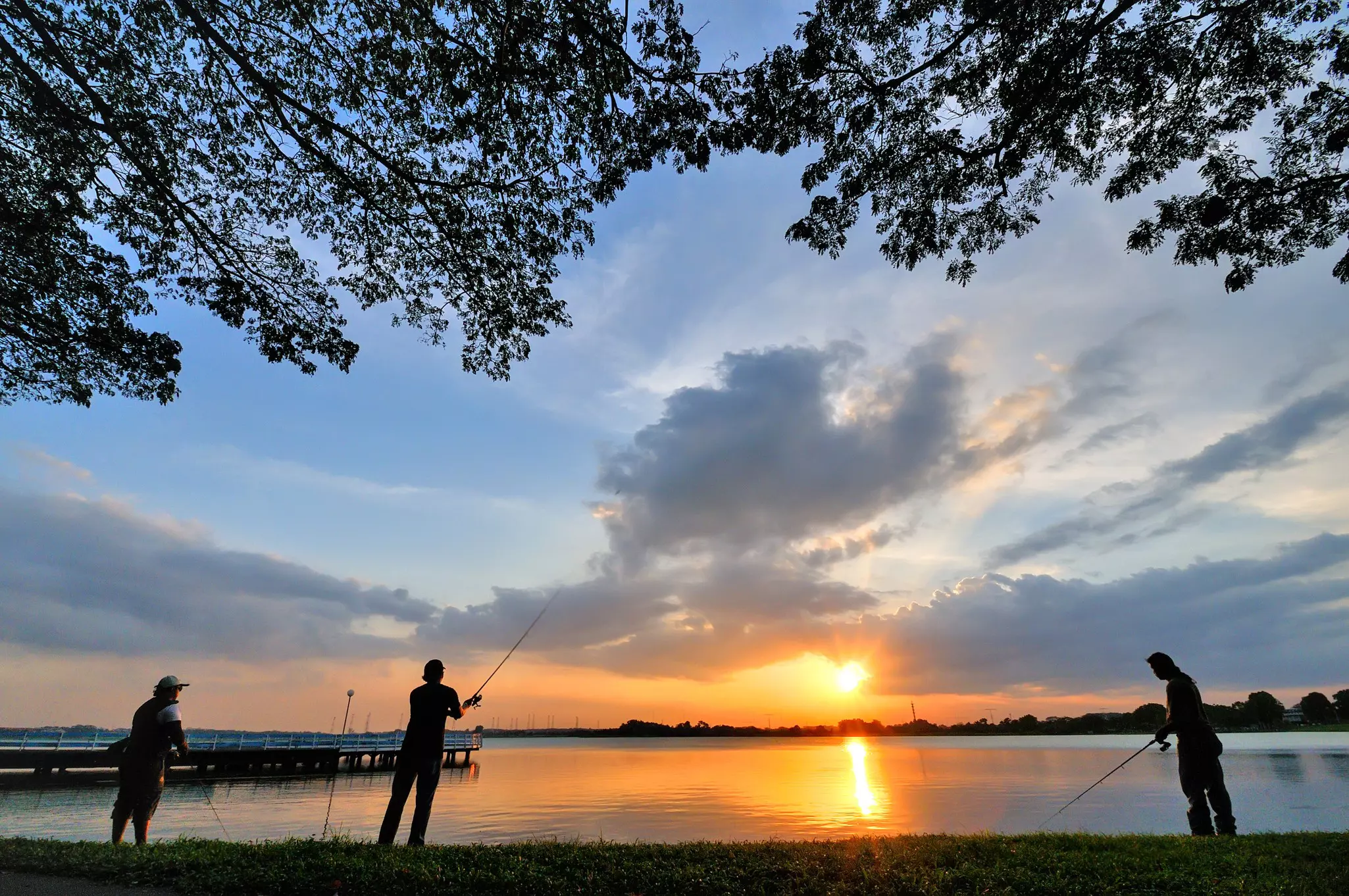 Three fishers at a calm lake at sunset.