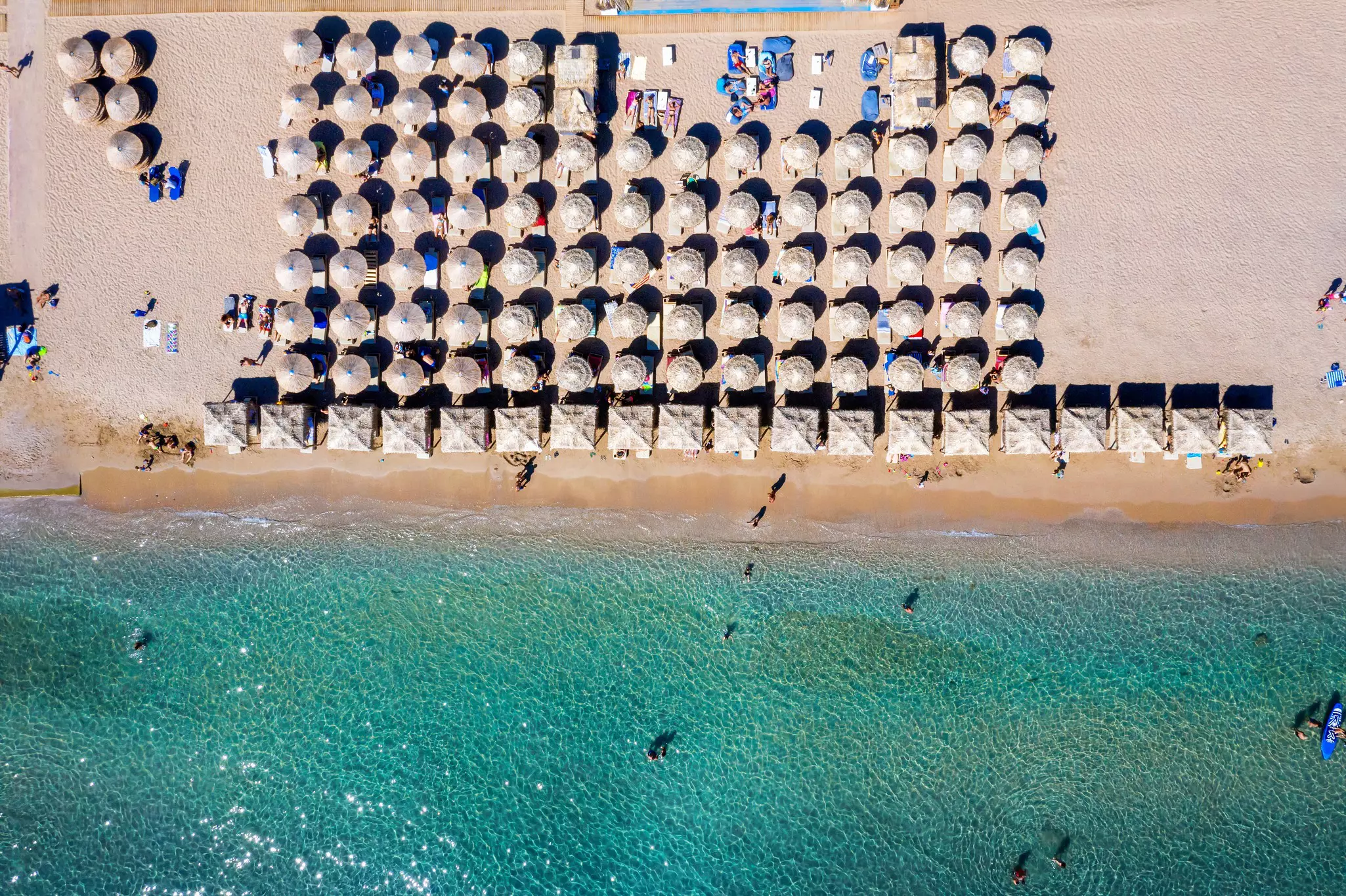 An overhead view of precisely aligned parasols and loungers on a beach