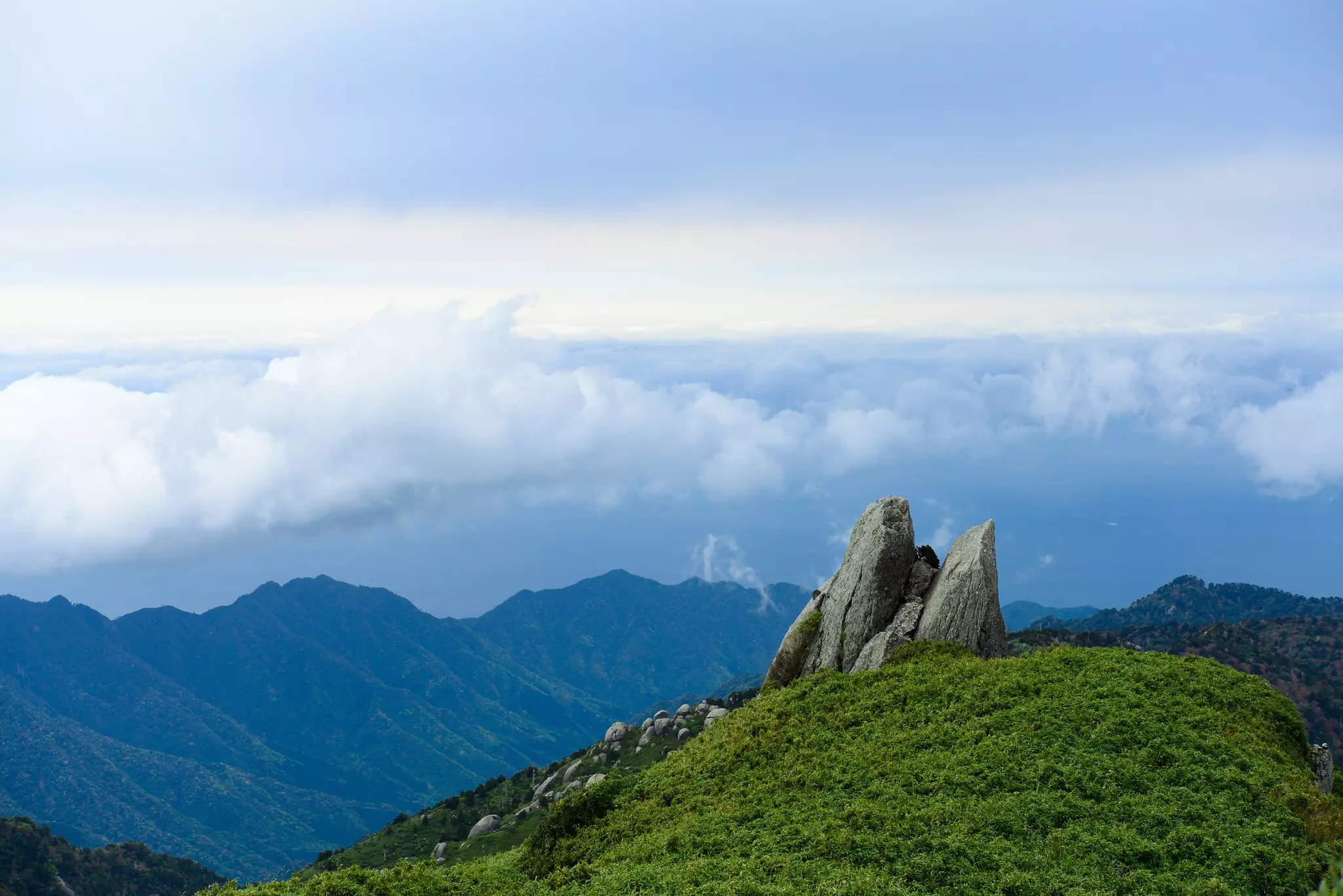 Clouds roll over the landscape viewed from the top of a mountain.