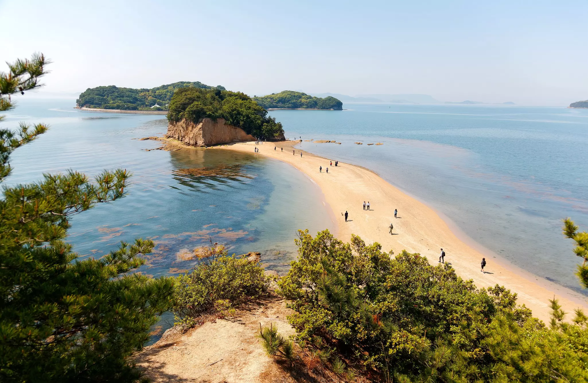 People wander on a tidal sandbar that gives access to a small rocky islet 