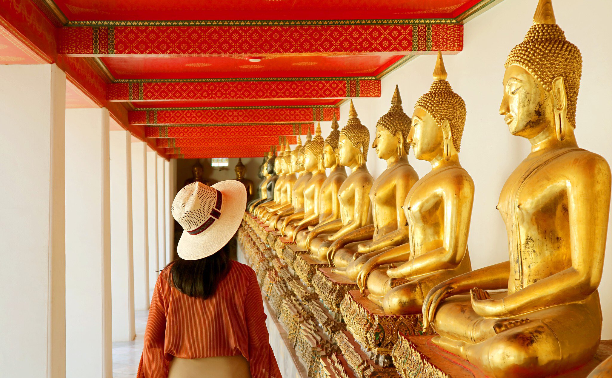 A woman walks past gilded statues of the Buddha at Wat Pho in Bangkok, Thailand. 