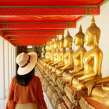 A woman walks past gilded statues of the Buddha at Wat Pho in Bangkok, Thailand. 