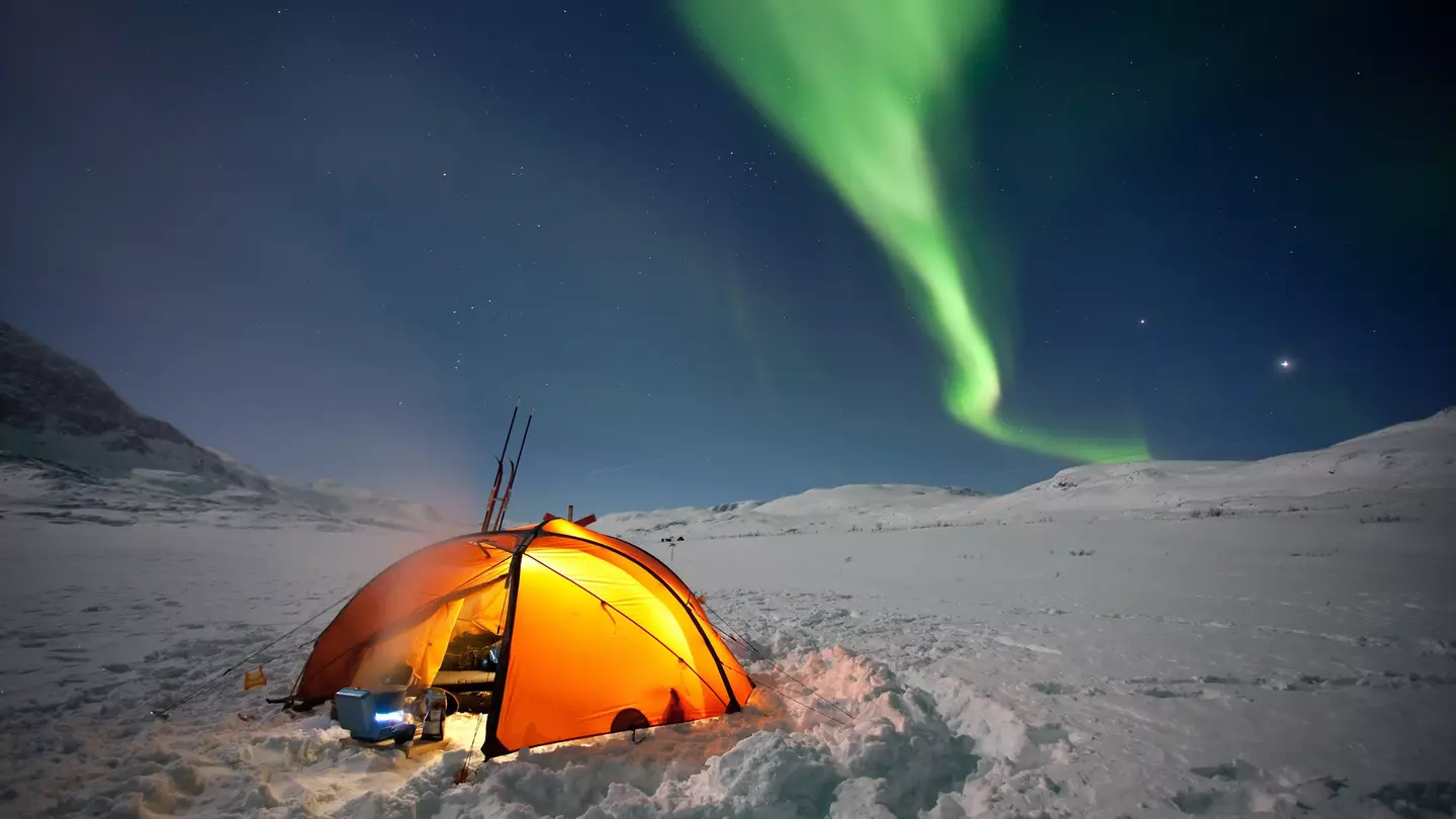 A tent in a snowy field under the Northern Lights in Sweden