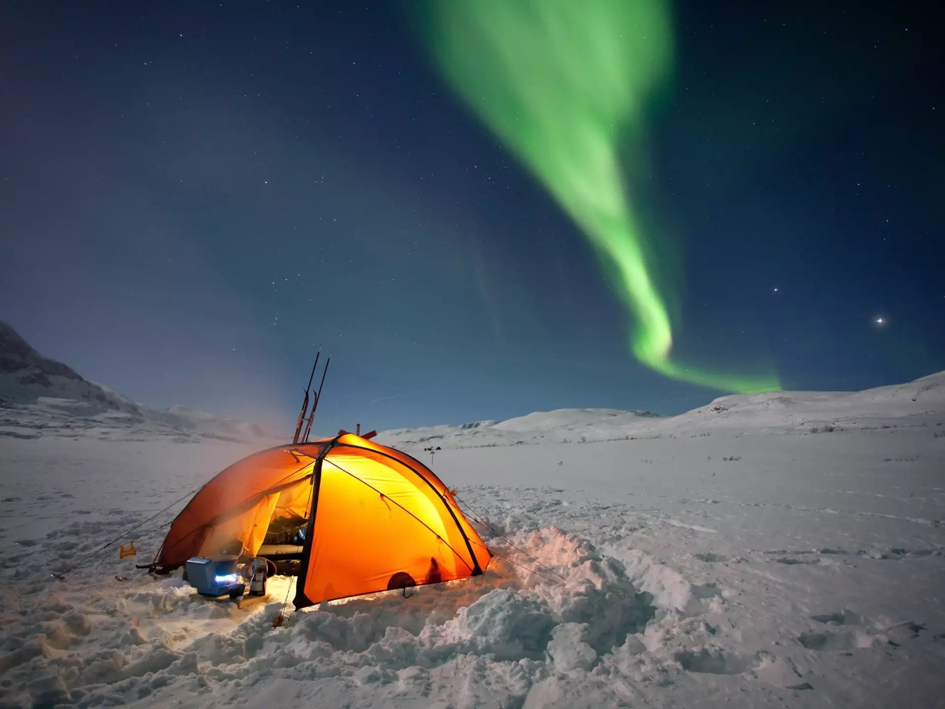 A tent in a snowy field under the Northern Lights in Sweden