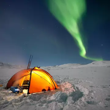 A tent in a snowy field under the Northern Lights in Sweden
