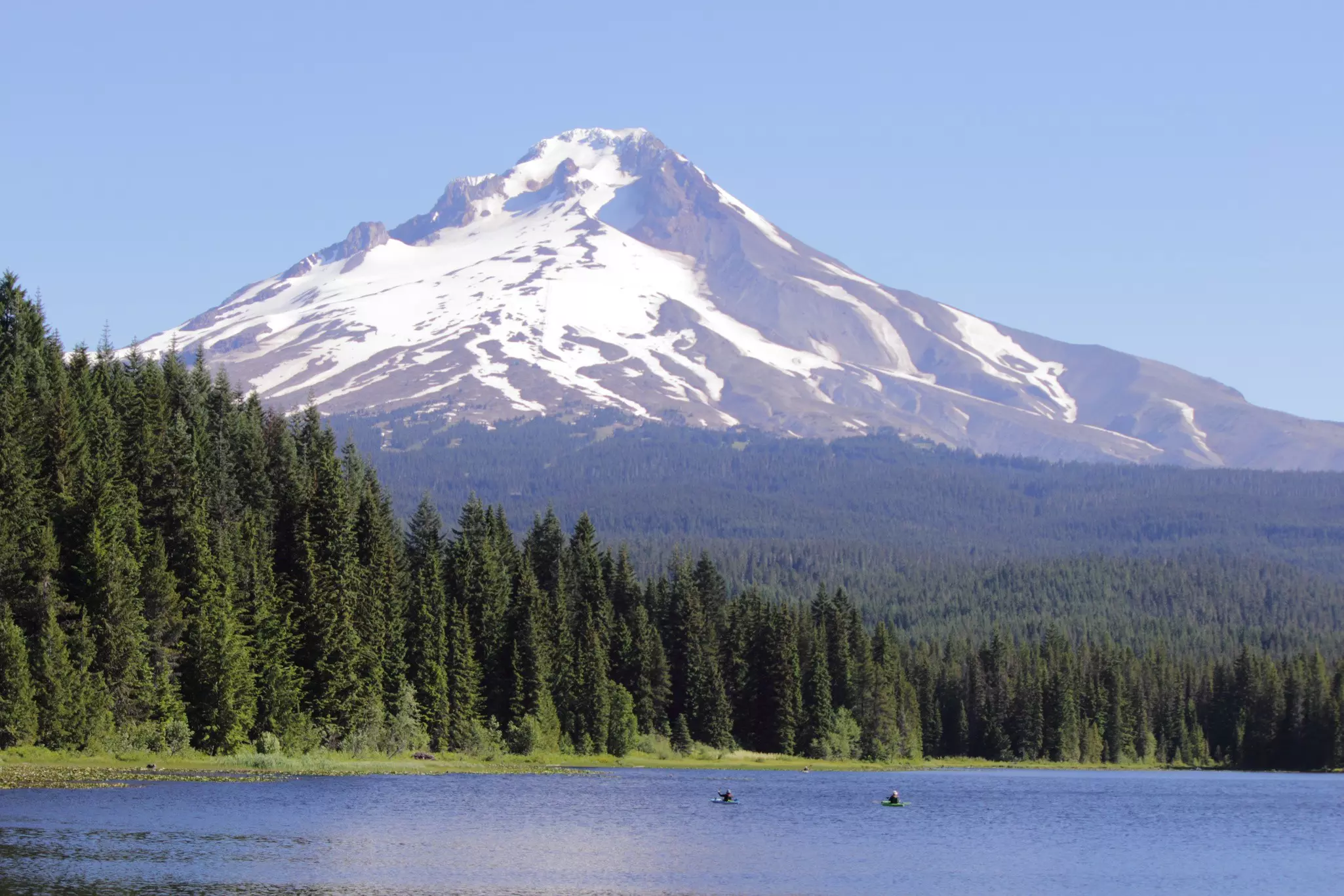 Two kayakers paddle in Trillium Lake with the snow-capped peak of Mt Hood beyond.