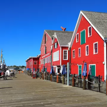 Bright red wooden buildings with white trim along a plank wharf, a fishing vessel tied up alongside