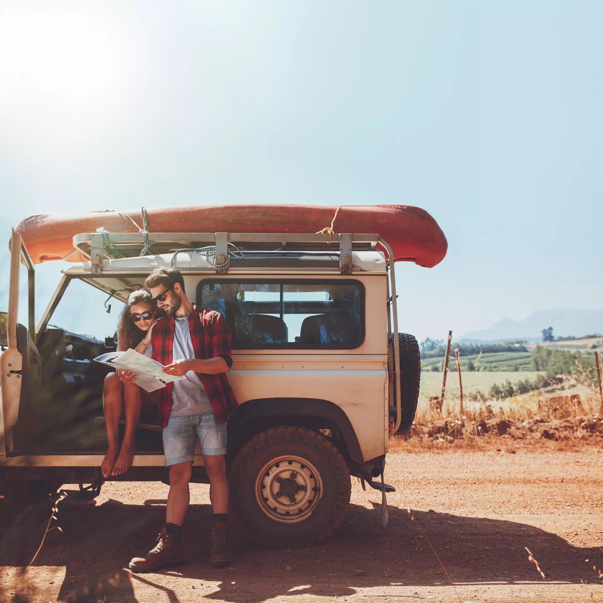 Young couple stopping on country road and looking at the map for directions. Man and woman on a road trip in countryside on a su