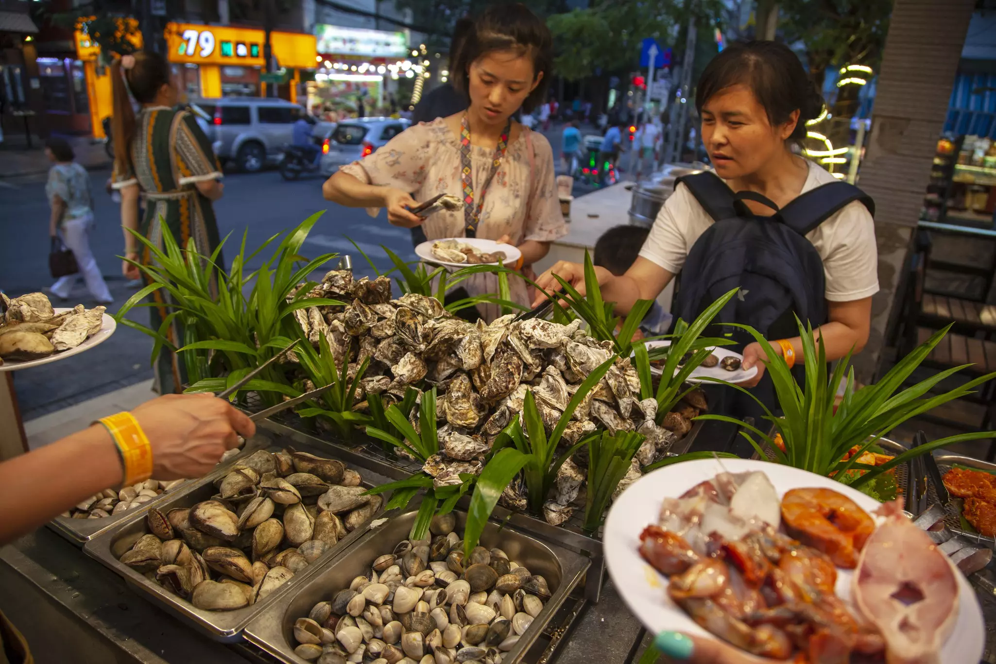 Women serve themselves helpings of seafood from a street vendor in a city.