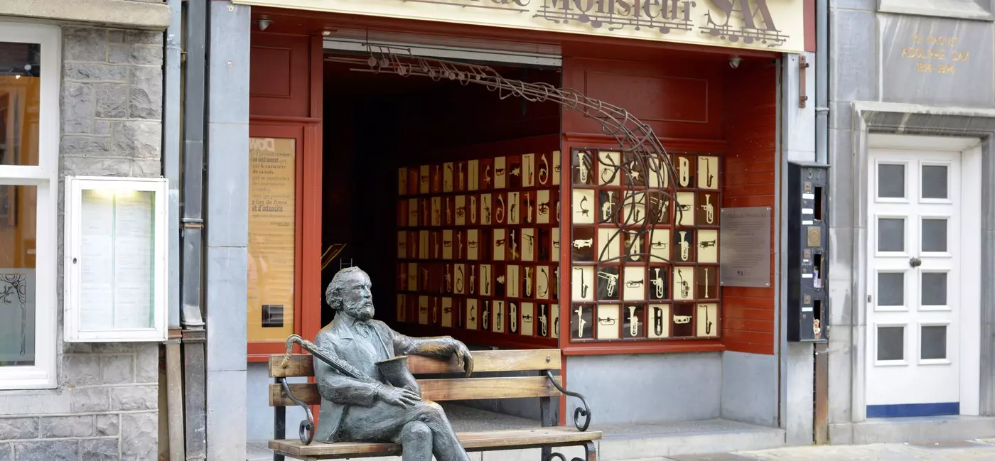 A commemorative bench on the street outside a decorative building with a bronze statues of a man holding a saxophone.