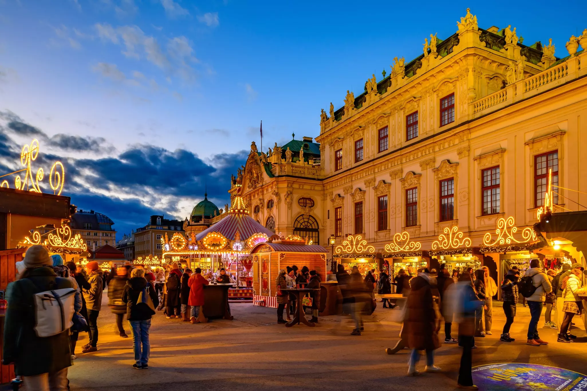 People wander among festive stalls outside a palace as dusk falls.