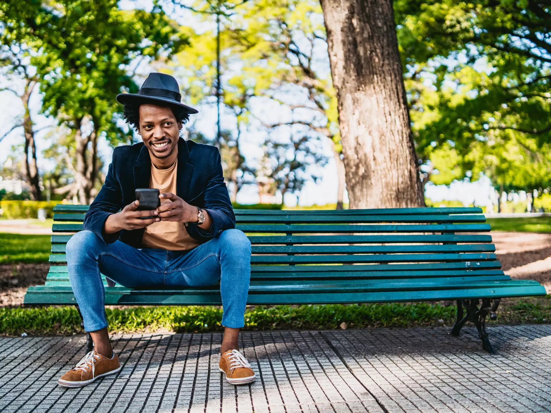 Smiling young African man using smartphone on park bench.
1216096777