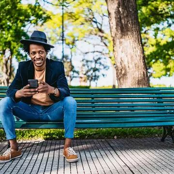 Smiling young African man using smartphone on park bench.
1216096777