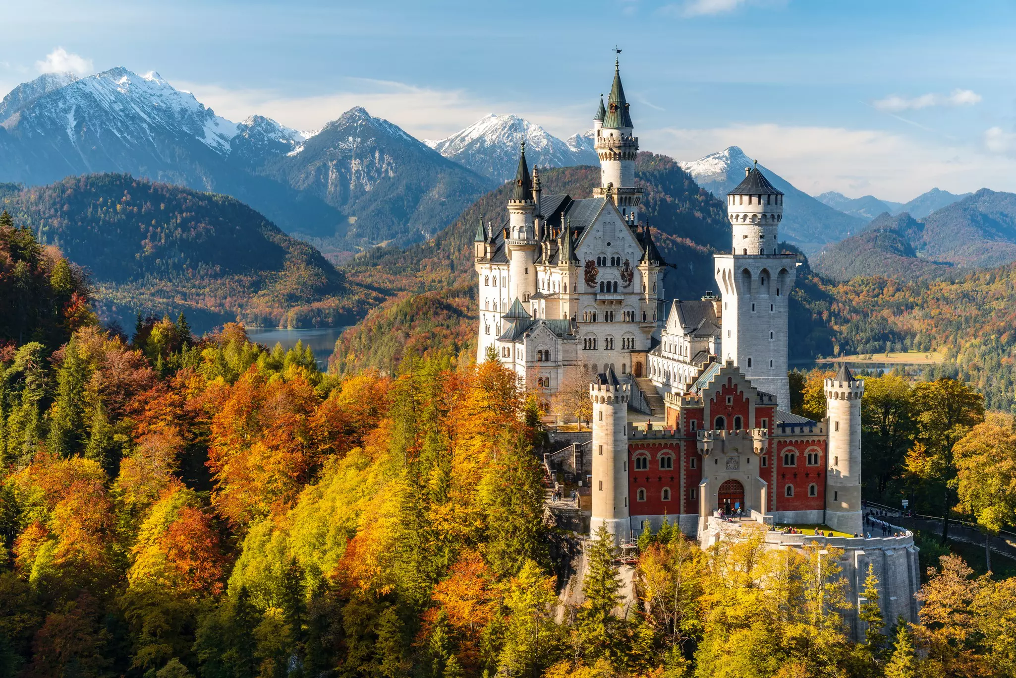 A castle with turrets is pictured in a landscape showing fall colors, with snowy mountains in the distance.