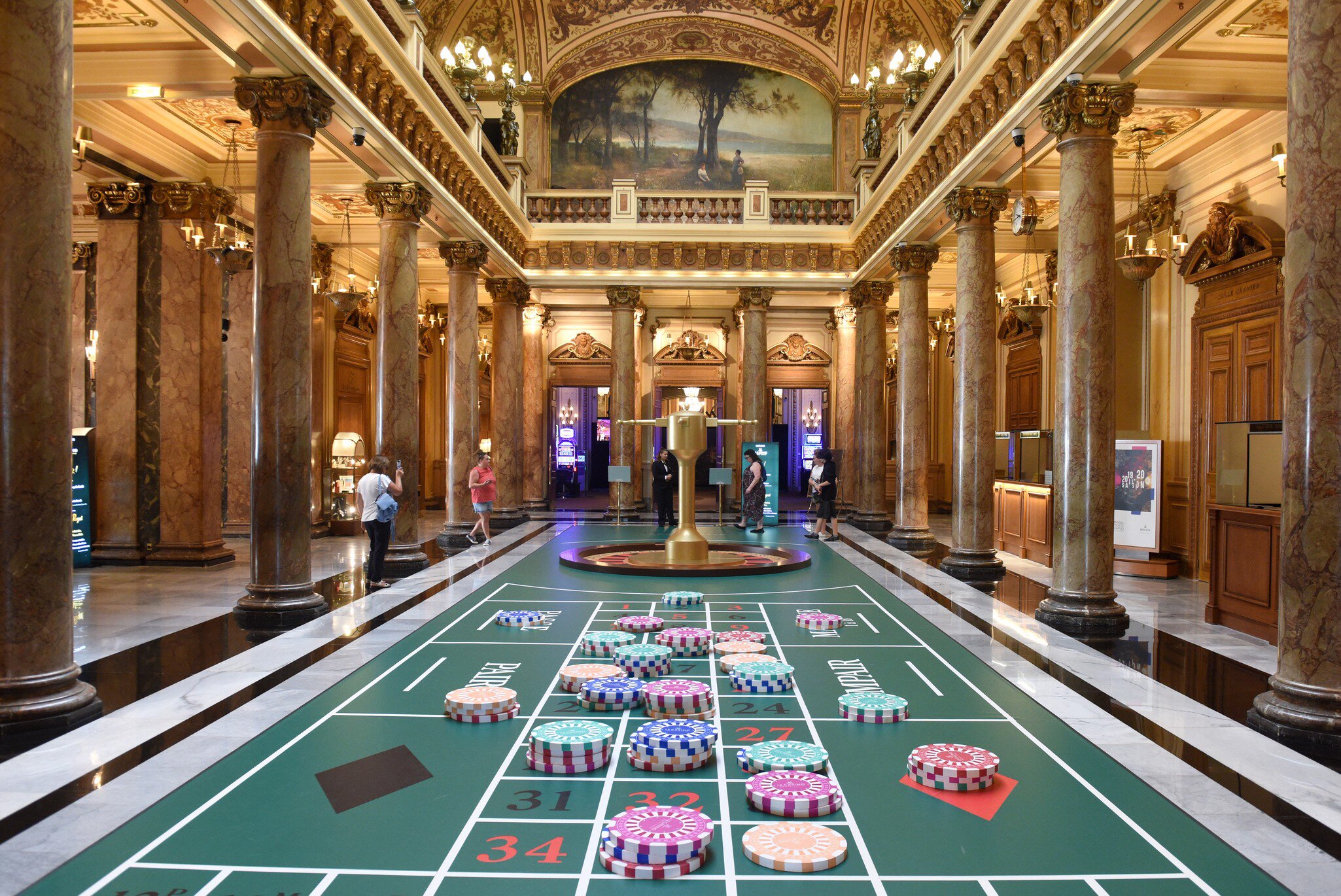 An ornate hall of marble columns beneath a gilded coffered ceiling and painted lunette.