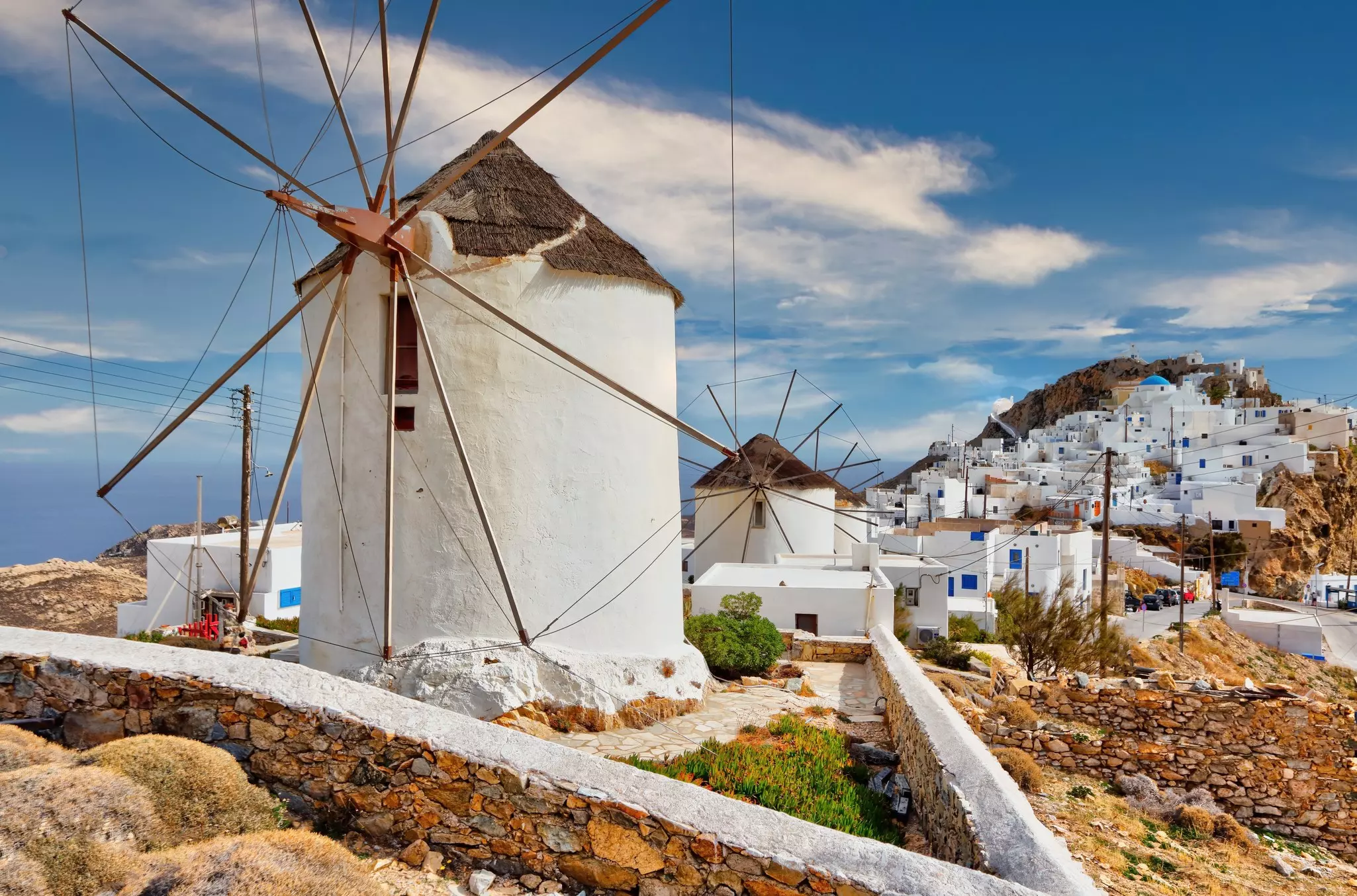 A large white windmill Smith white buildings in the background and sky with clouds