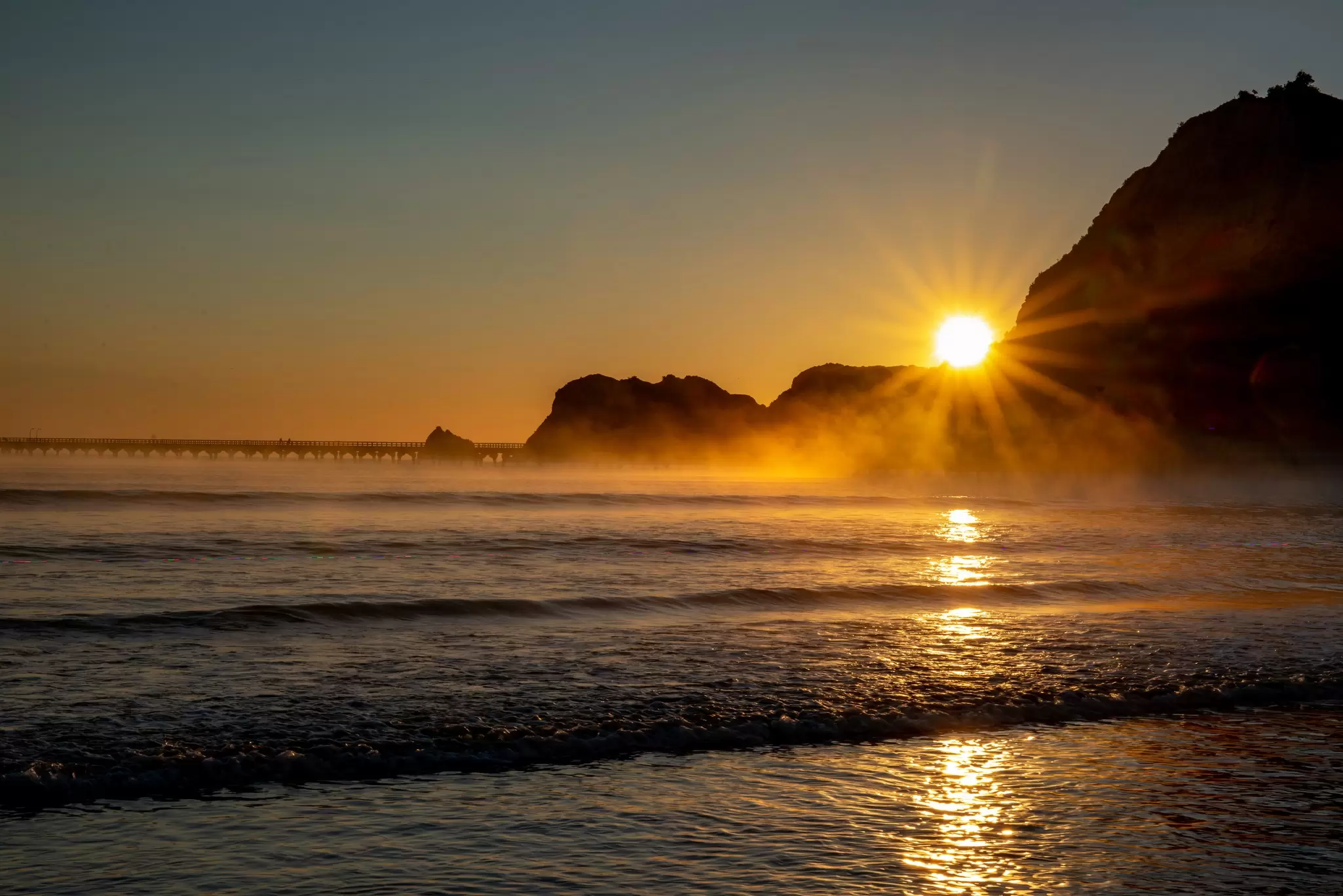 Sunrise over a rock formation at an ocean beach.