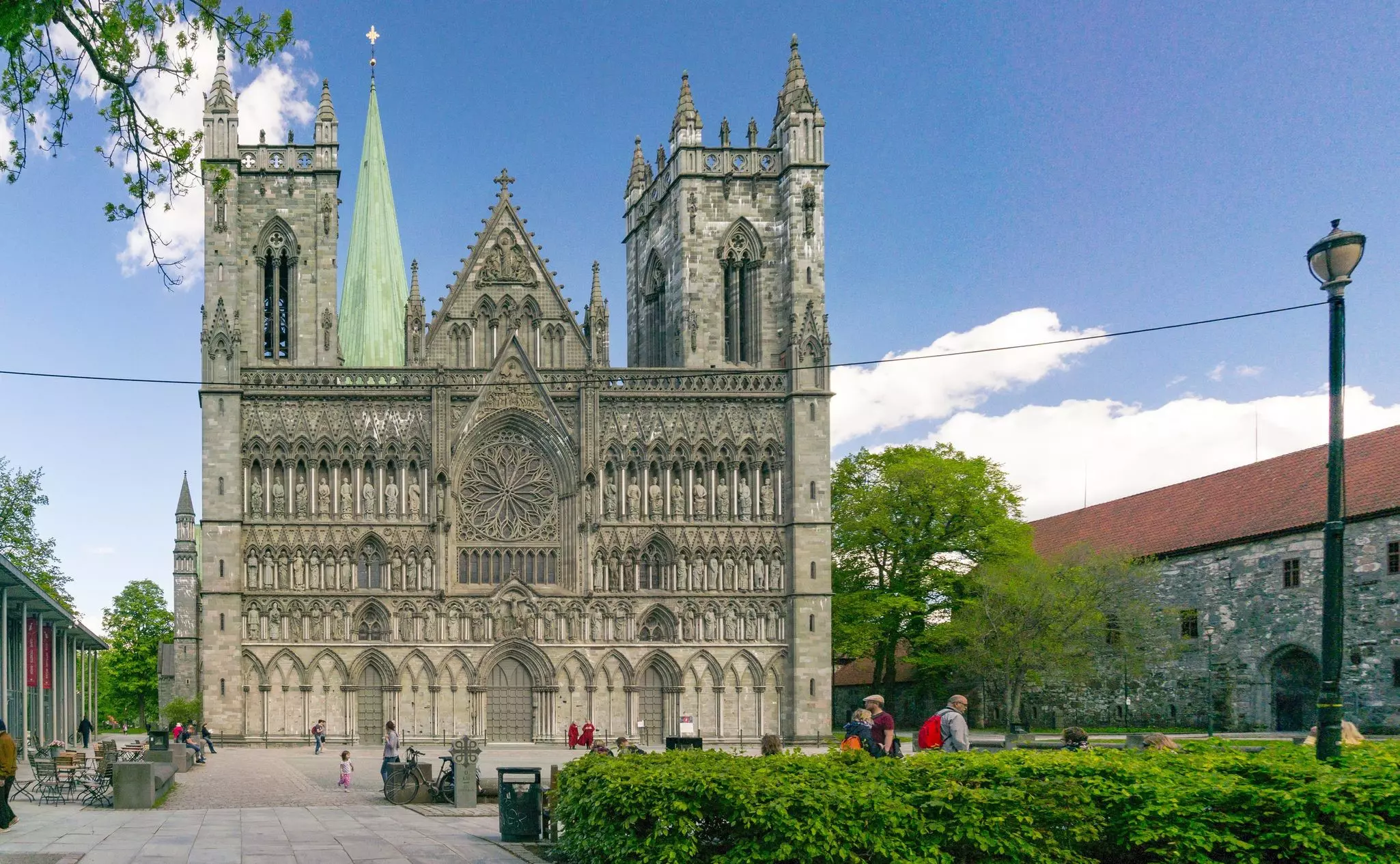 The ornately carved facade of the cathedral in Trondheim is pictured in front of a square with bushes.