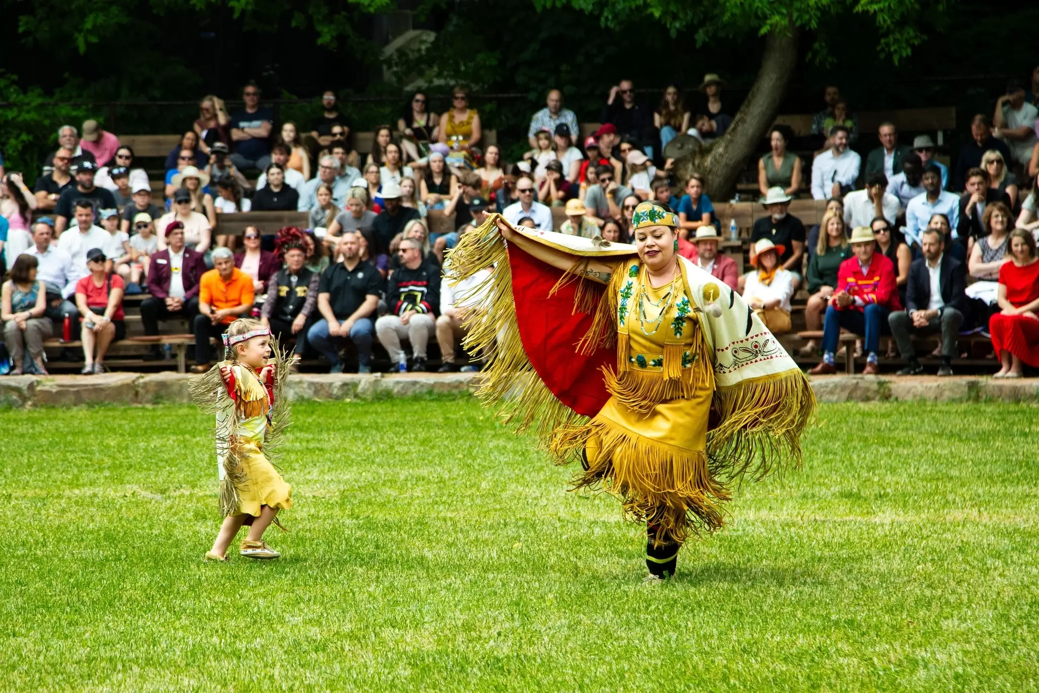 A woman and boy in traditional Indigenous dress perform for spectators on a lawn in Wendake, Québec, Canada