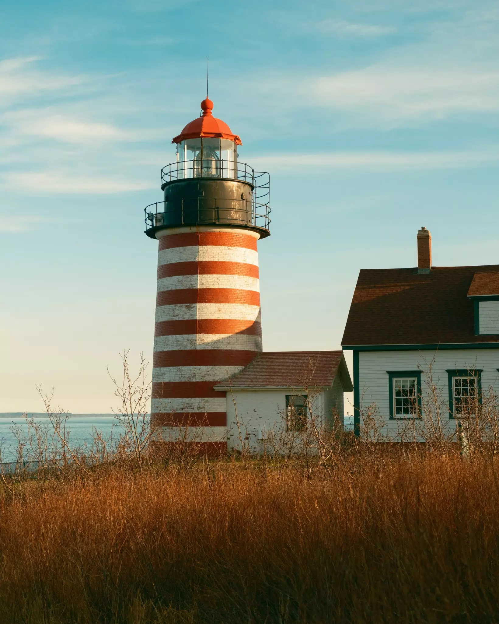 A lighthouse with red and white stripes next to a coastal cottage