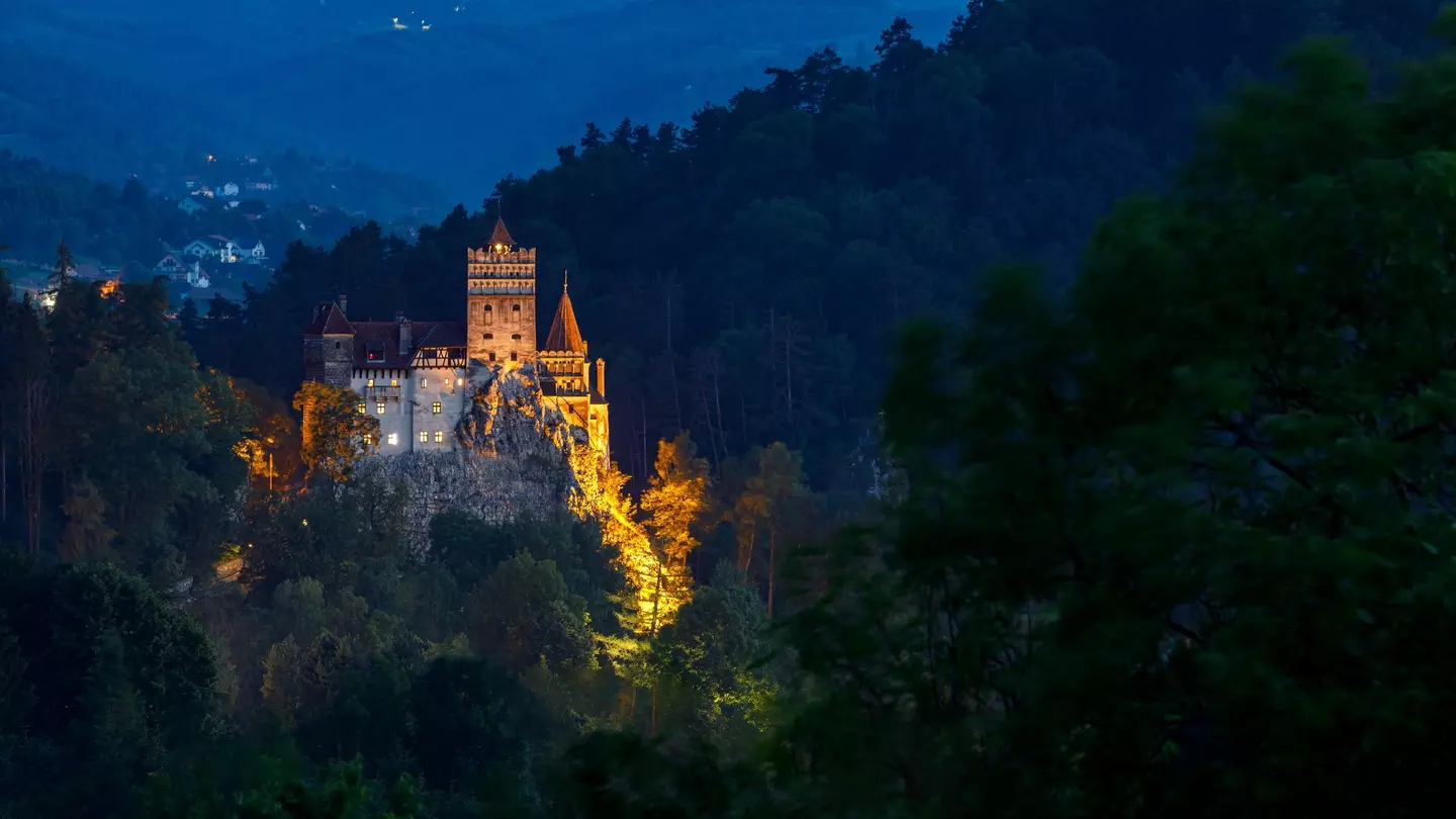 A view of a castle on a cliff top illuminated by night among shadowy hillsides