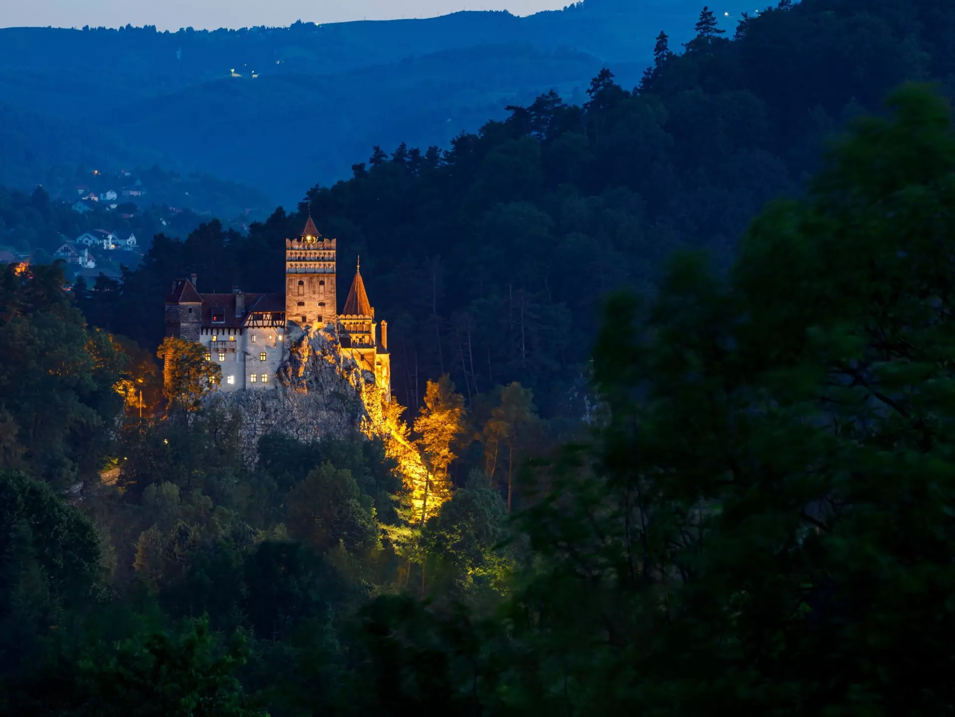 A view of a castle on a cliff top illuminated by night among shadowy hillsides