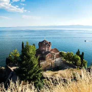 The red-roofed Church of St John at Kaneo stands among cypress trees on a hill above the blue water of Lake Ohrid