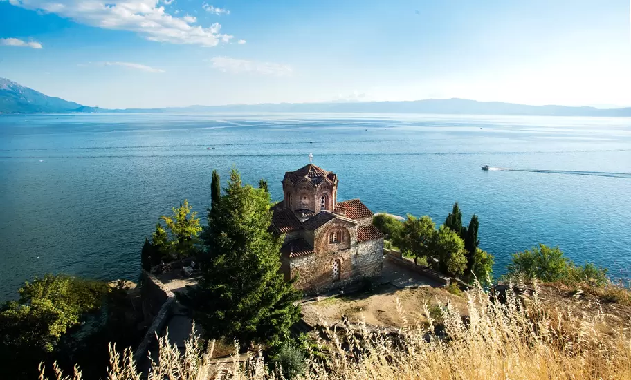 The red-roofed Church of St John at Kaneo stands among cypress trees on a hill above the blue water of Lake Ohrid
