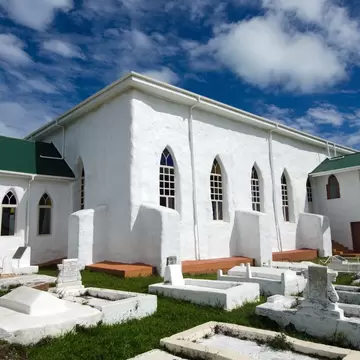A whitewashed church with a green tin roof and pointed windows, standing among whitewashed tombs on cut grass.