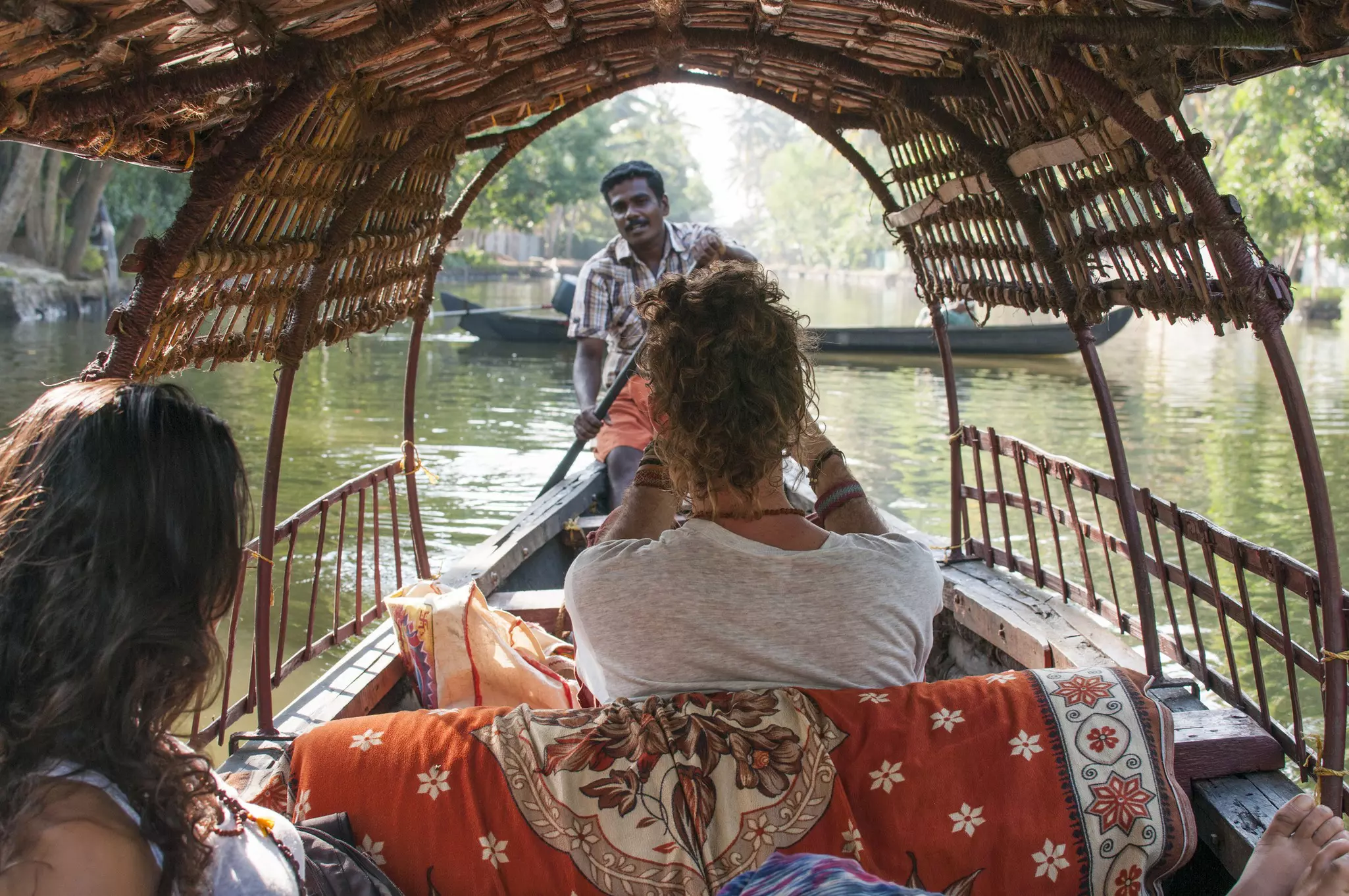 Two women ride in a wooden boat that's low to the water and being piloted by a man
