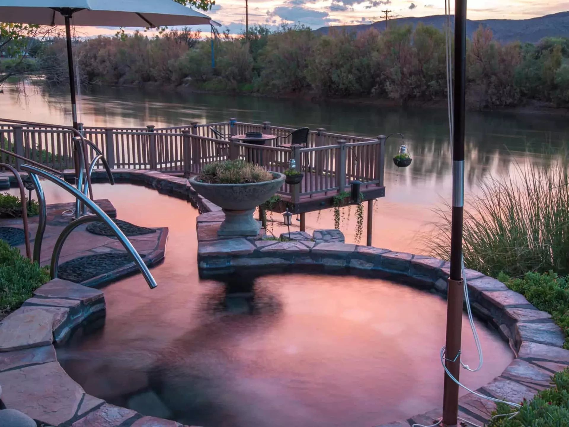 A small round pool right beside a river at sunset.